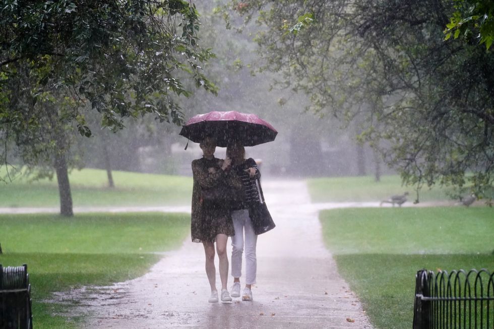 Two women walks through heavy rain in St James's Park in central London. Thunderstorms bringing lightning and torrential rain to the south are set to continue until Monday, forecasters have said. Picture date: Sunday July 25, 2021.