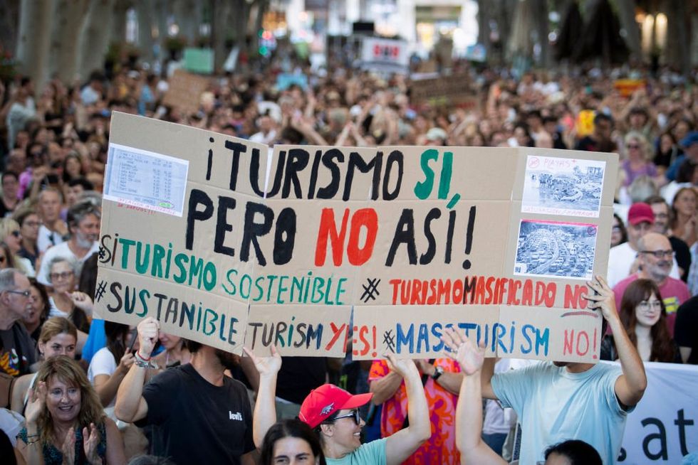 \u200b People hold a placard which reads as 'Tourism yes, but not like this'