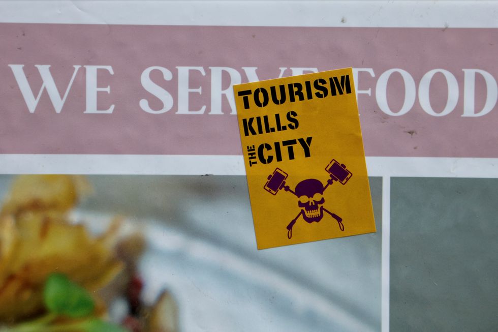 \u200b'Tourism kills city' reads a sticker stuck on a restaurant's banner