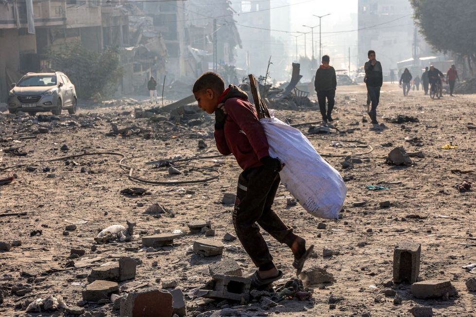 \u200bA boy walks with a sack of salvaged items through debris at the site of Israeli bombardment on a residential block in Jalaa Street in Gaza City