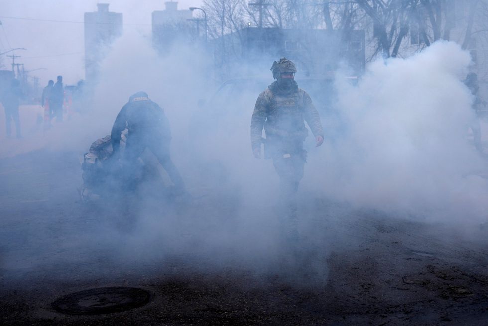 \u200bA federal agent walks as others hold a person down while being surrounded by tear gas used to deter protesters,