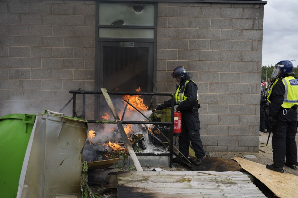 \u200bA fire is extinguished by police officers as trouble flares during an anti-immigration protest outside the Holiday Inn Express