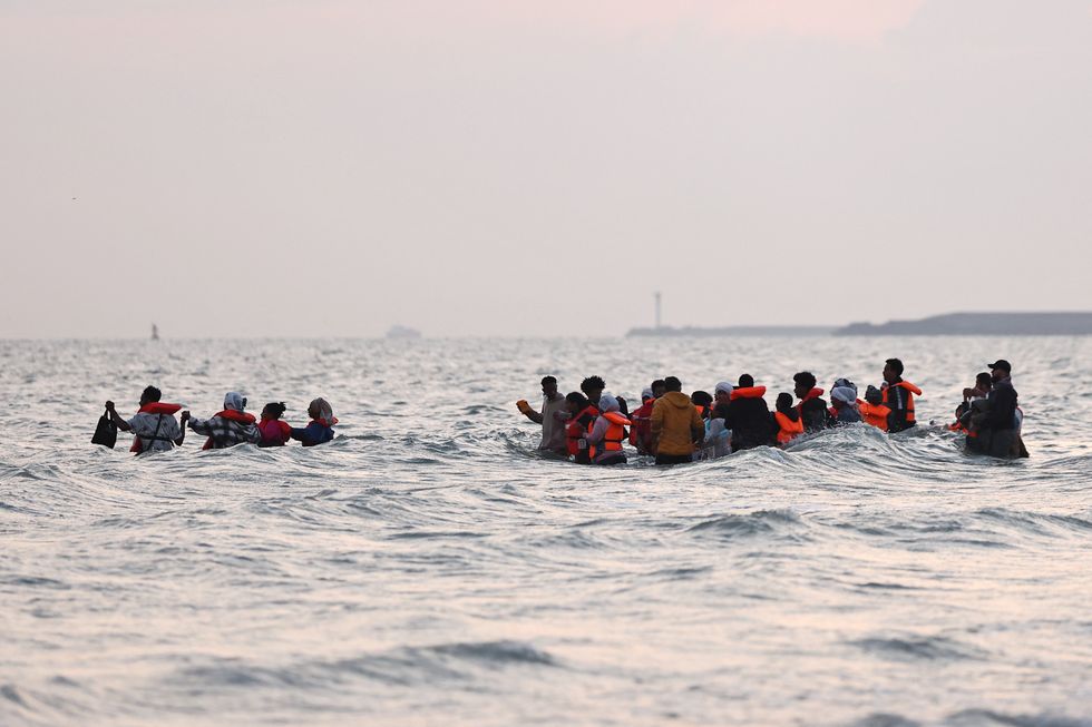 \u200bA group of migrants walk through the water to reach an inflatable dinghy in an attempt to cross the English Channel