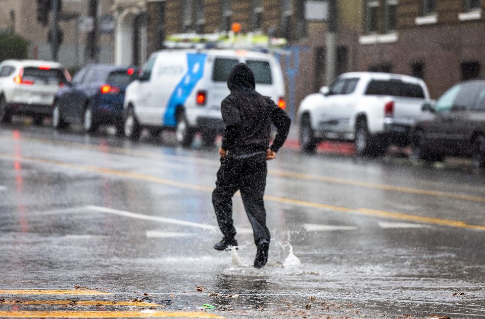 \u200bA pedestrian runs through puddles crossing the street amid rain showers in downtown Los Angeles Monday, January 22