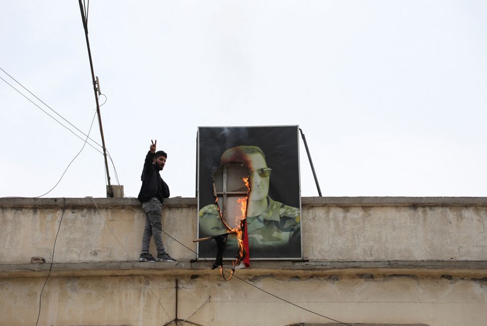 \u200bA person gestures next to a burning picture of President Bashar al-Assad, after rebels seized the capital and ousted the president