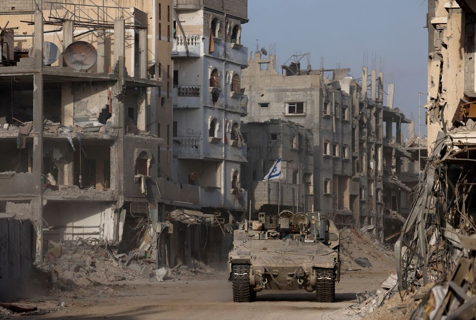 \u200bAn armoured vehicle drives as damaged buildings are seen in the background, amid the ongoing ground operation of the Israeli army against Palestinian Islamist group Hamas, in the Gaza Strip
