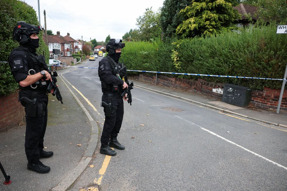 \u200bArmed police officers stand guard by a road with houses near the synagogue in Manchester