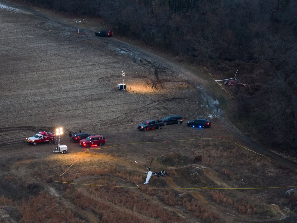 \u200bEmergency vehicles can be seen parked between the remains of a white and red helicopter