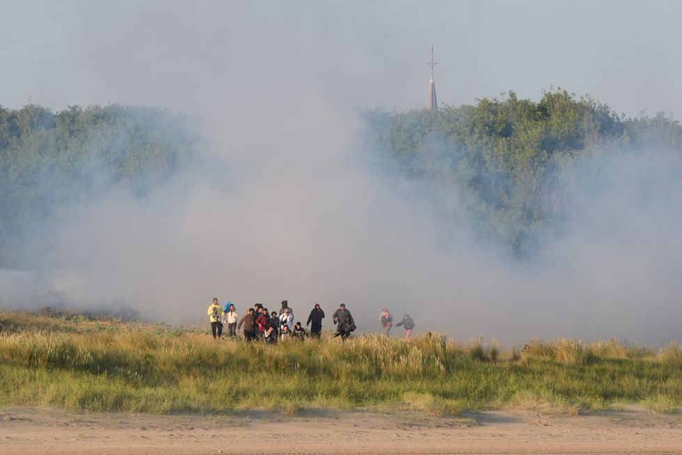 \u200bMigrants emerge from bushes on a beach in Gravelines, France, after French authorities had fired tear gas