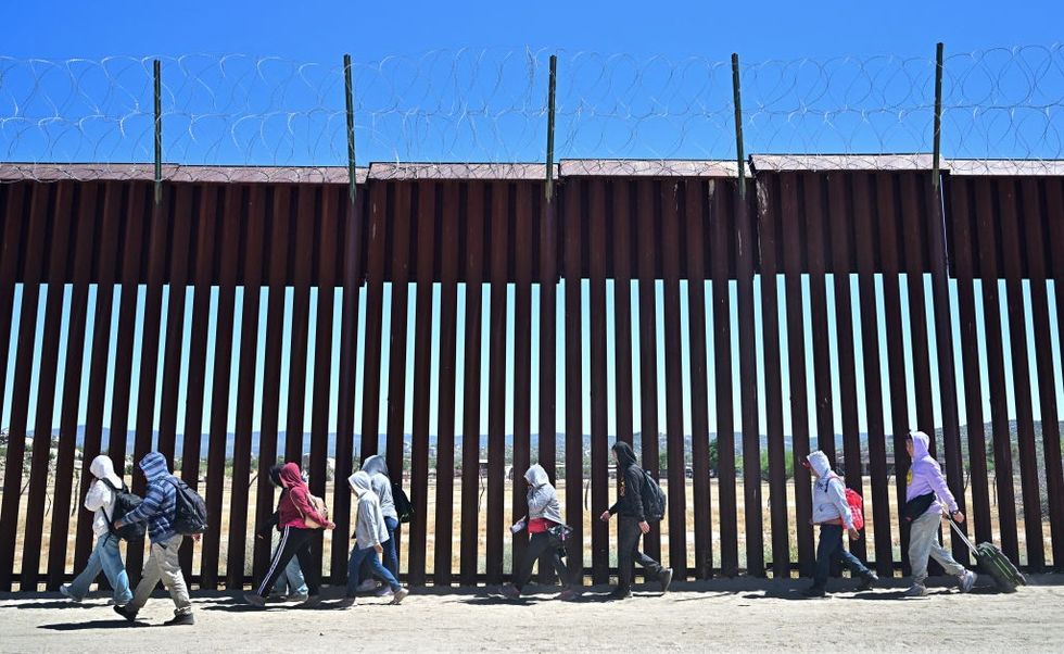 \u200bMigrants walk on the US side of the border wall in Jacumba Hot Springs, California