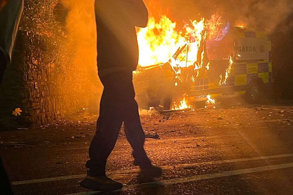 \u200bOnlookers watch a police vehicle burning in Dublin