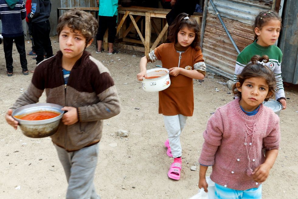 \u200bPalestinian children walk after receiving food cooked by a charity kitchen