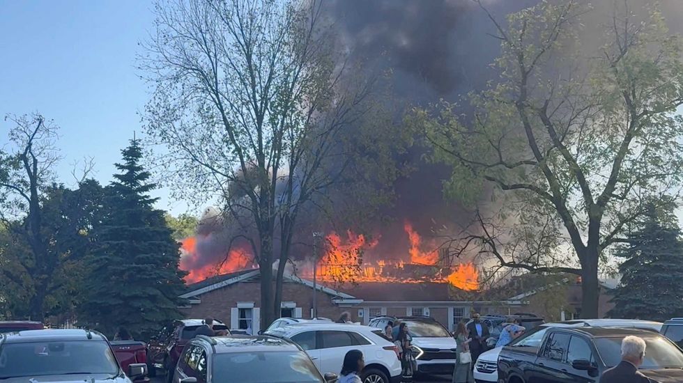 \u200bPeople gather at the site as smoke and fire rise, following an incident in which a man crashed his vehicle through the front doors of a Michigan church and opened fire with an assault rifle