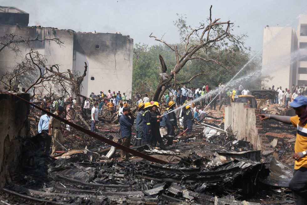 \u200bPeople gather near a damaged building and trees as firefighters work at the site where an Air India plane crashed in Ahmedabad