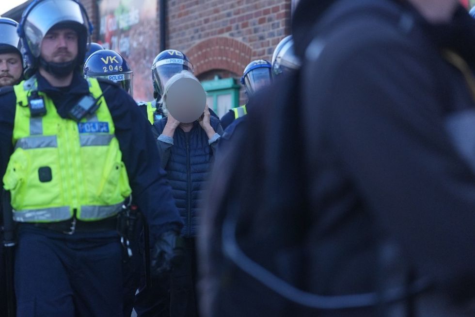 \u200bPolice officers escort a woman away from a demonstration for her own safety, after a protest outside a suspected migrant hotel in Epping, Essex