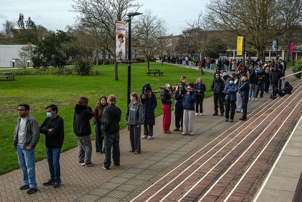 \u200bStaff and students, some wearing face masks, queue to receive antibiotics at the University of Kent in Canterbury