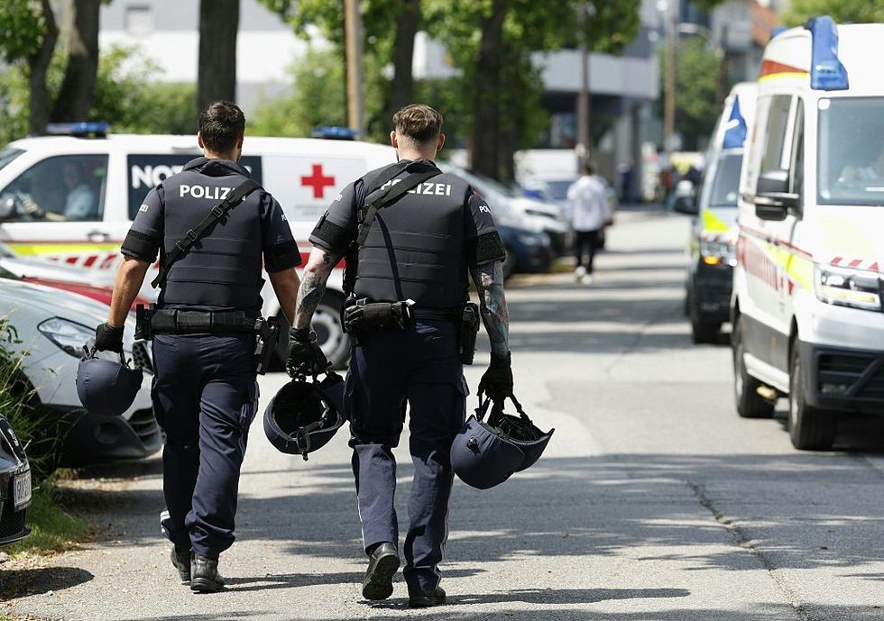 \u200bTwo policemen walk past ambulance cars in a street close to a school
