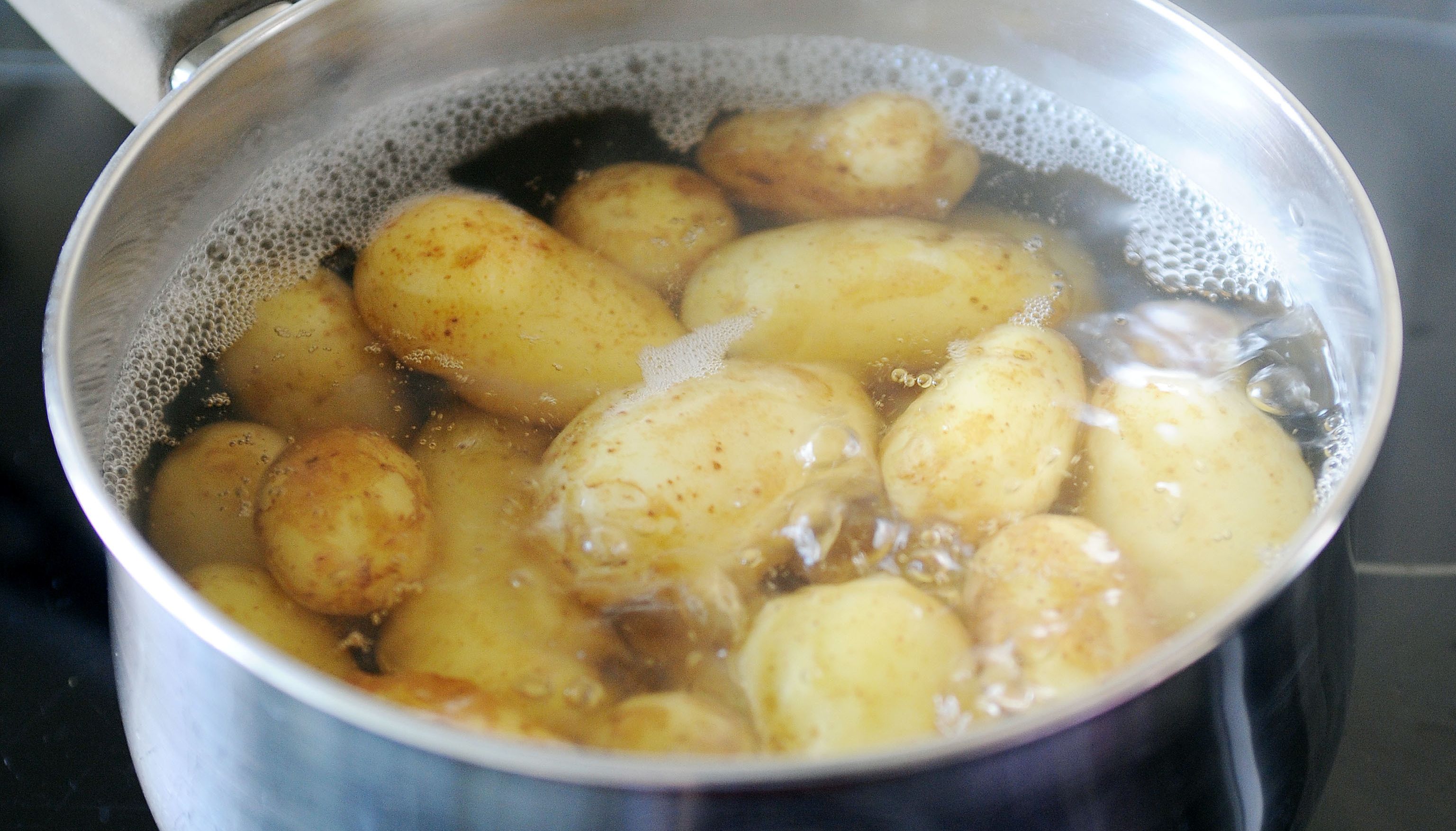Vegetable stock photo of baby new potatoes cooking in a pan of water on an electric hob.