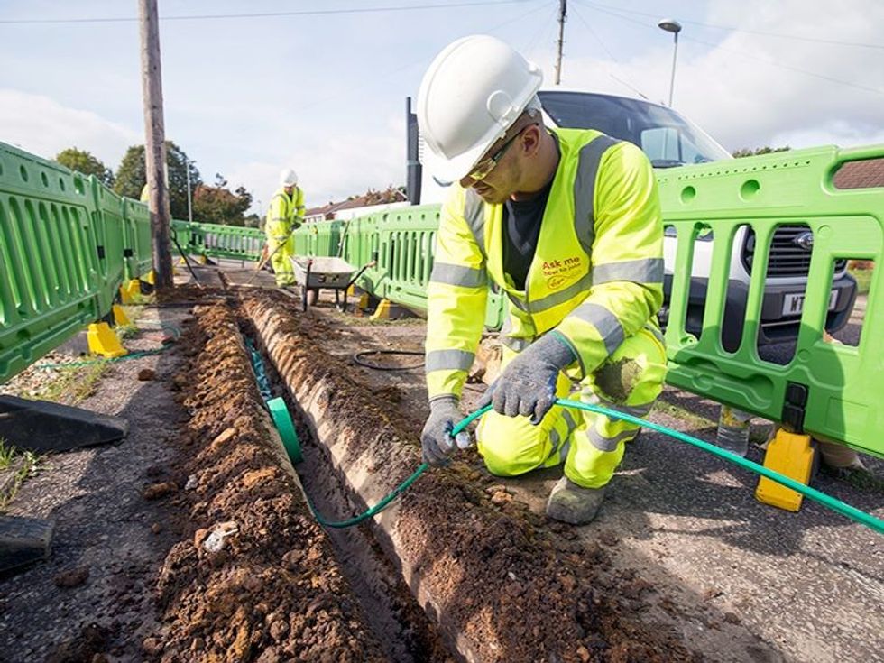 virgin media engineer in uniform pulling out a fibre-optic cable from the ground