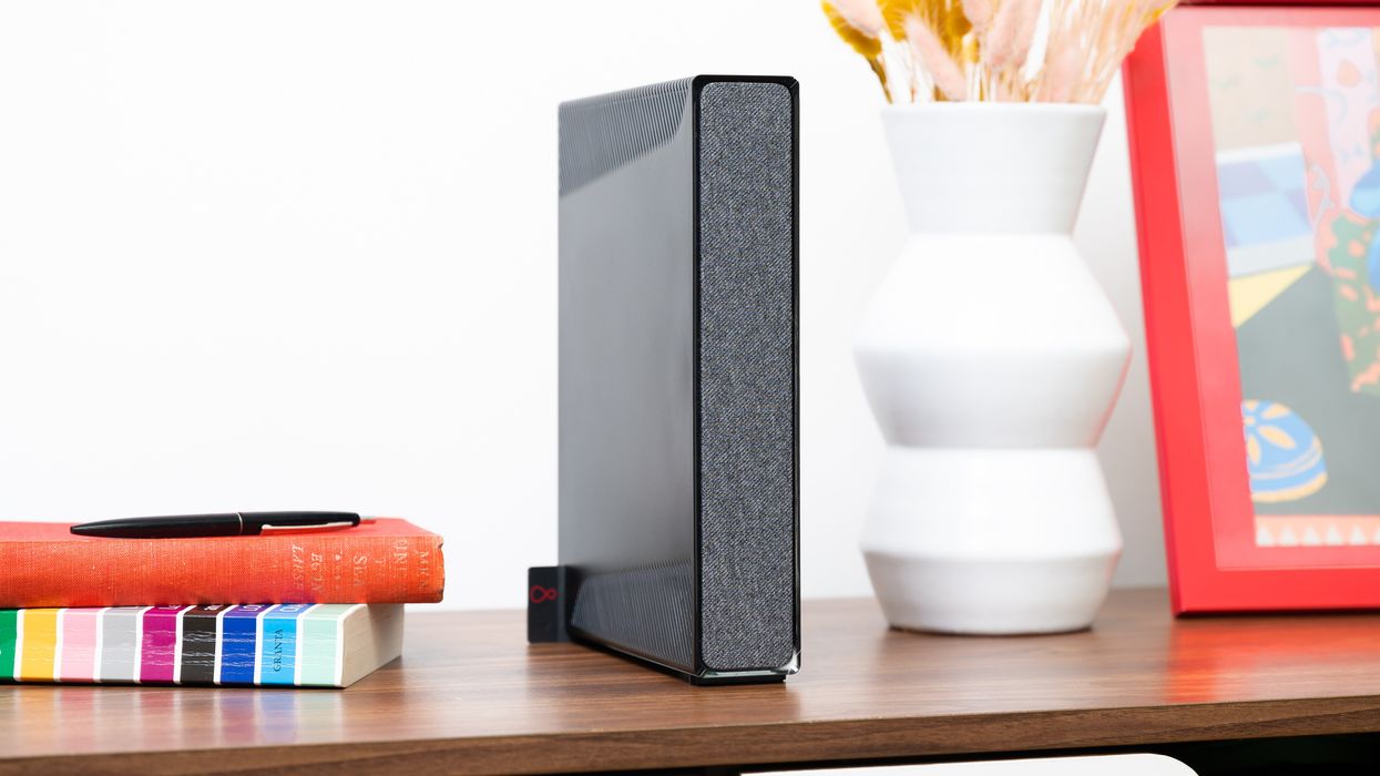 virgin media hub 5 wi-fi router is pictured on a wooden shelf with dried flowers and photo frames nearby