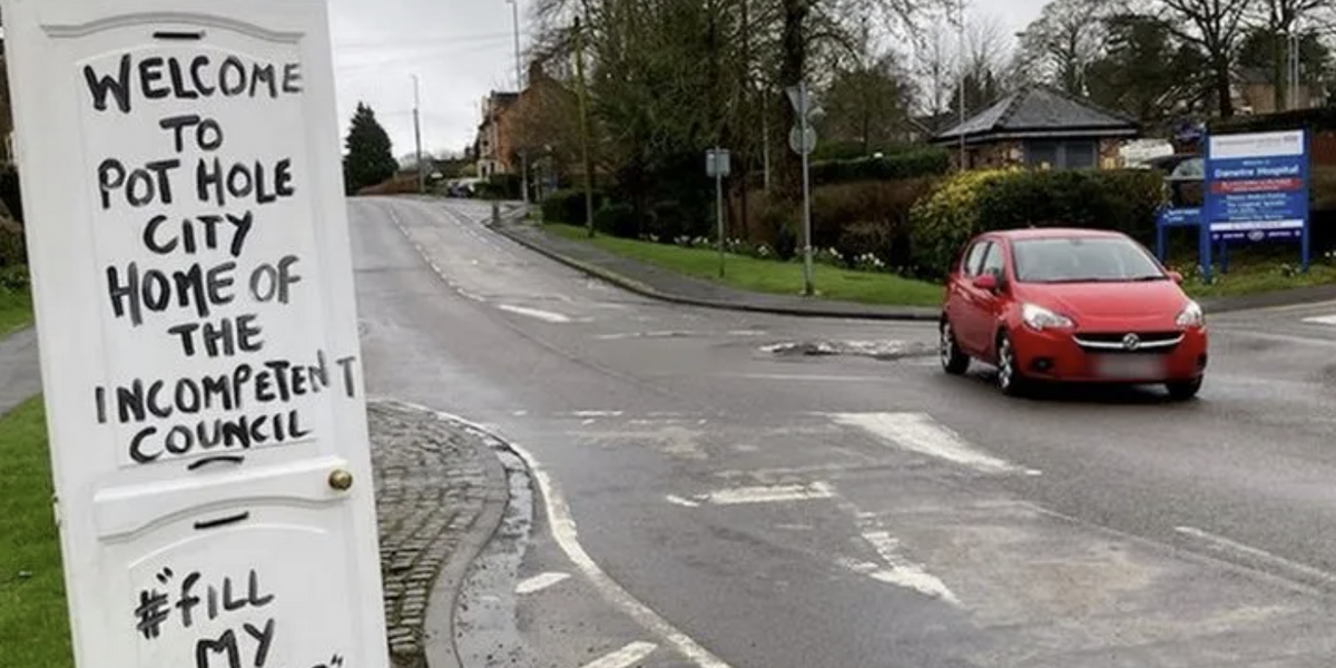NextImg:Mystery sign writer mocks council for devastating potholes and vows not to stop until he gets an apology