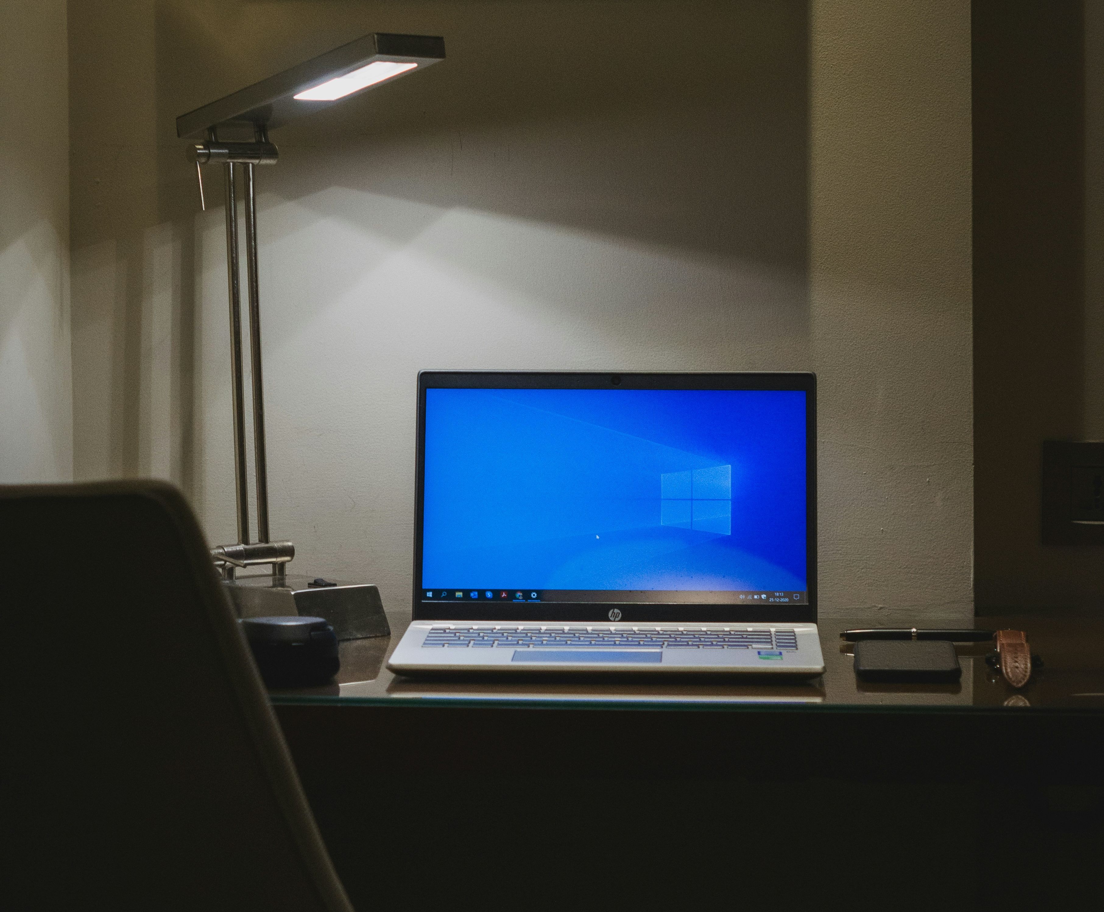 windows 10 laptop sat on a desk lit by a lamp