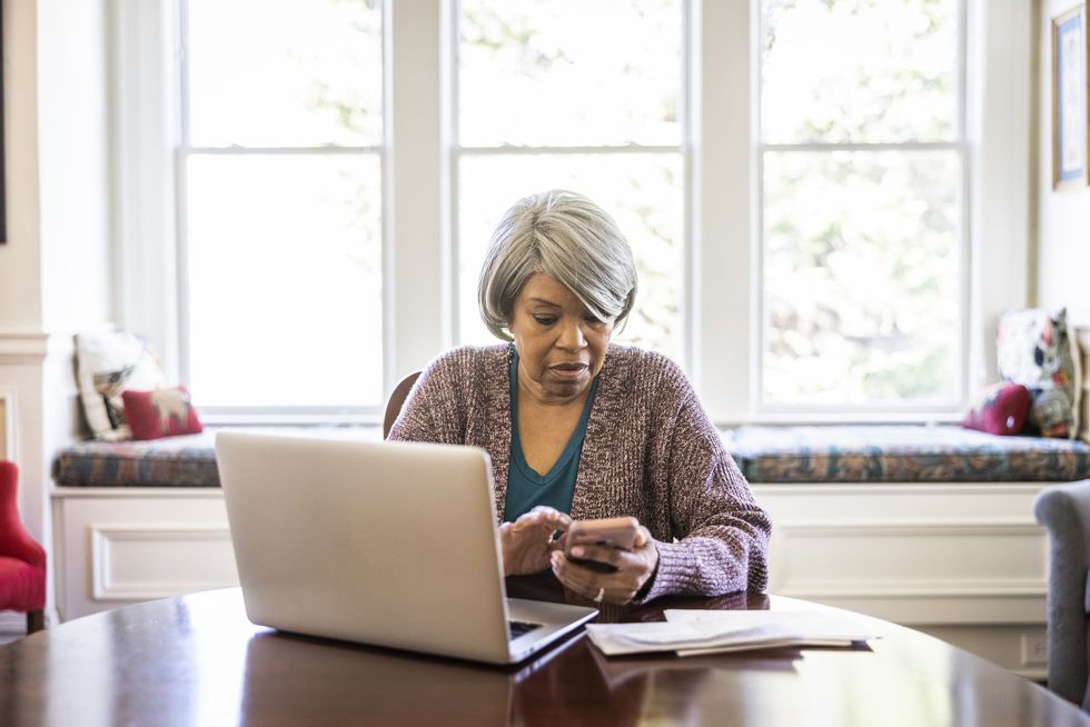 Woman at laptop looking at her phone