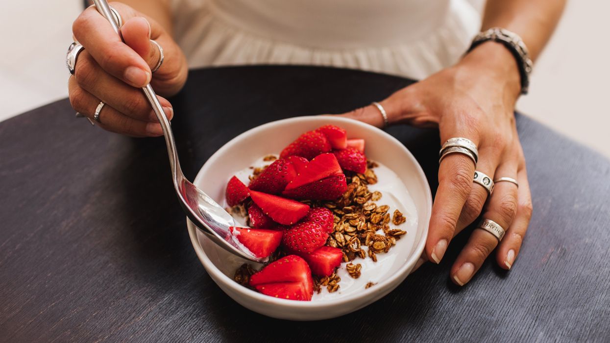 Woman eating bowl of granola, fruit, and yoghurt