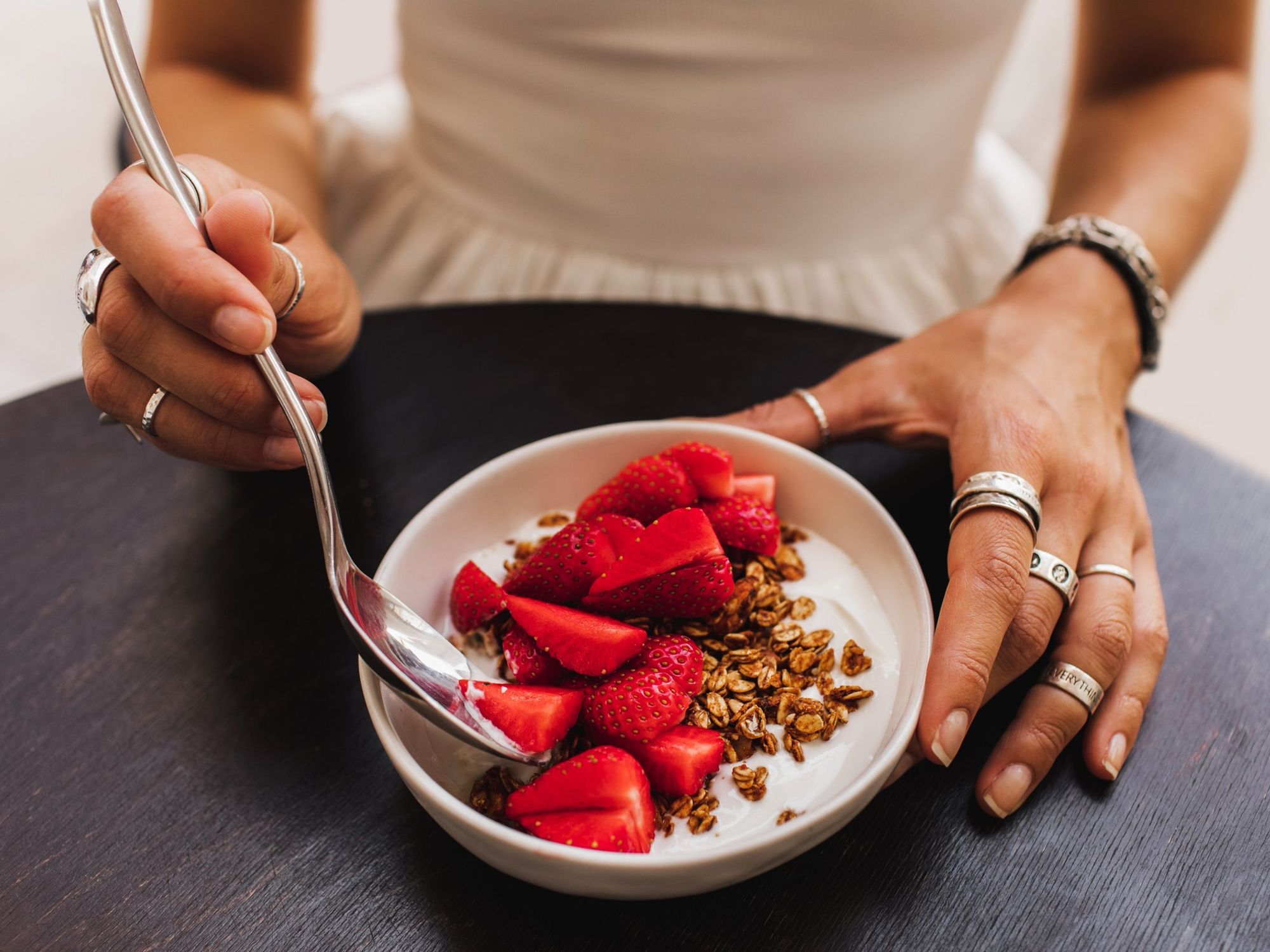 Woman eating bowl of granola, fruit, and yoghurt
