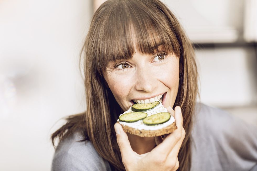 Woman eating slice of whole grain bread with cucumber topping