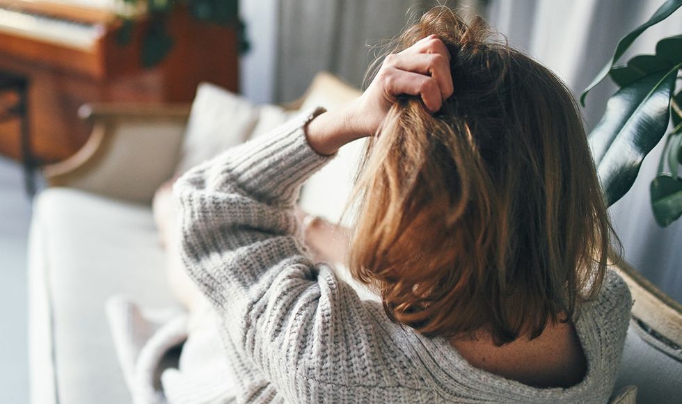 Woman gripping her head in pain on her sofa
