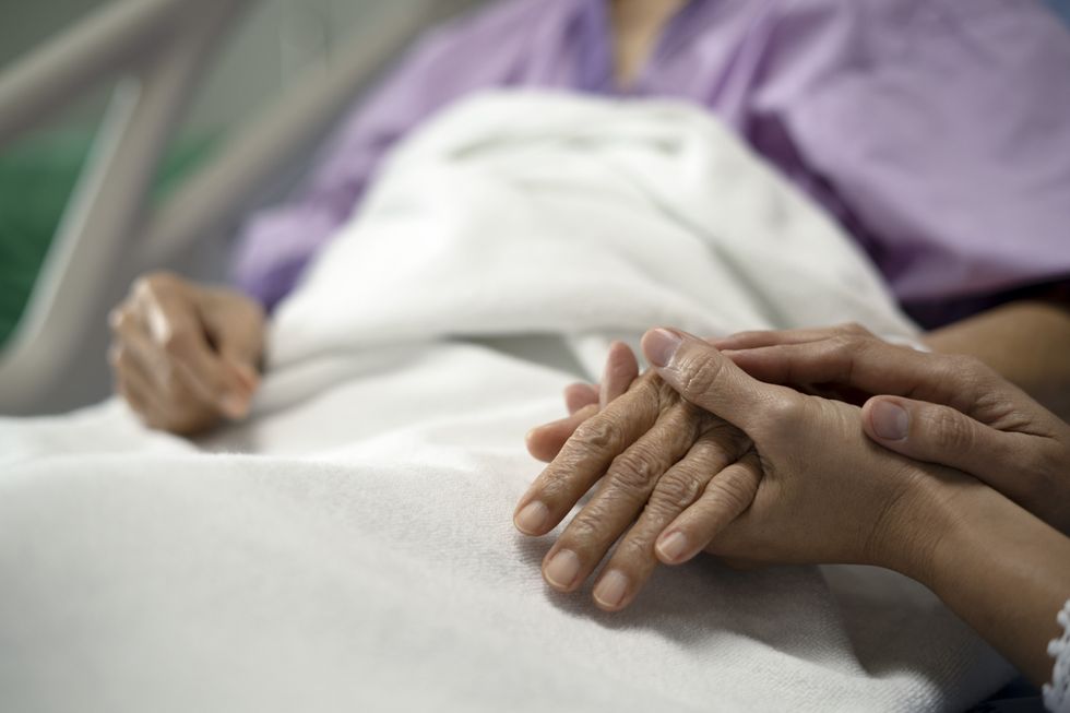 Woman holding the hand of an elderly person in bed