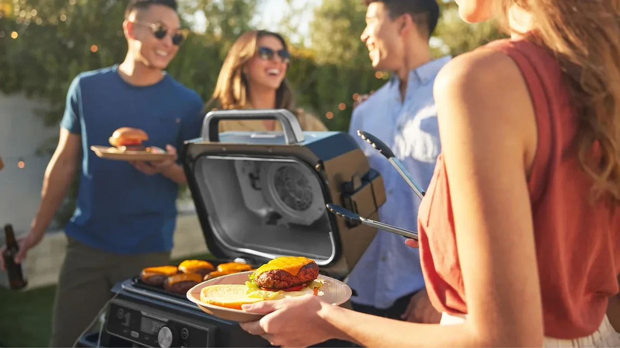 woman holds a beef burger and bun on a plate with the ninja outdoor bbq cooking