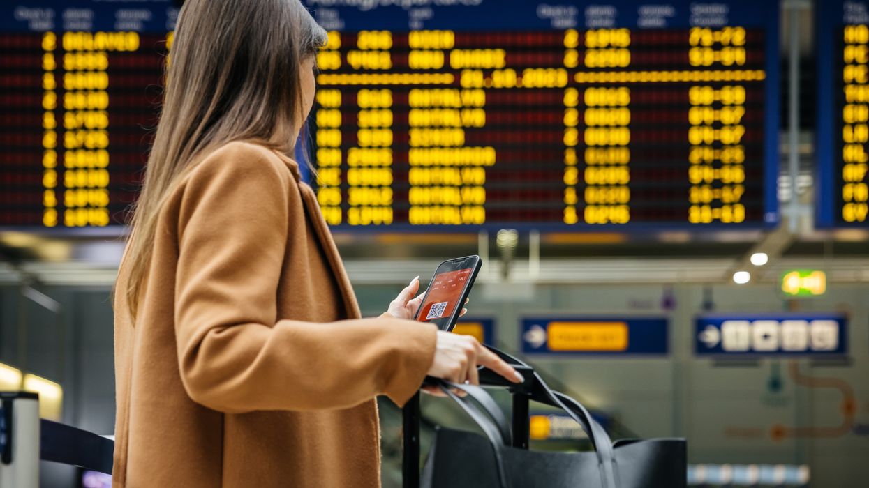 woman holds her smartphone with her bags at the airport ahead of a flight