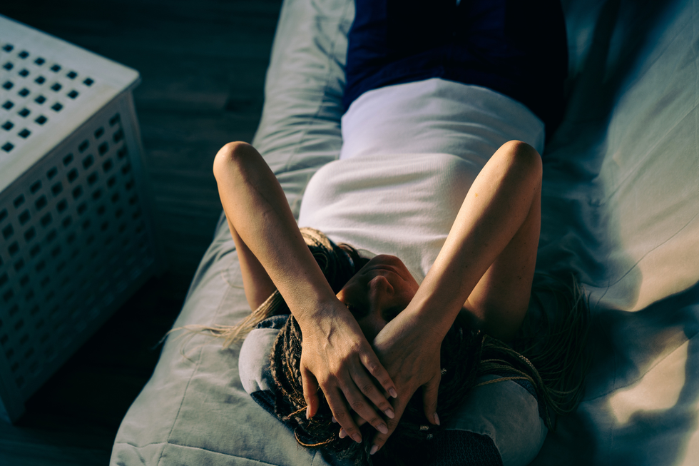 Woman in a white t-shirt lying down holding her hands to her head