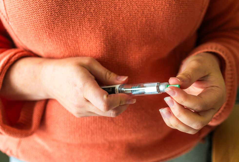 Woman in an orange jumper holding a weight loss pen