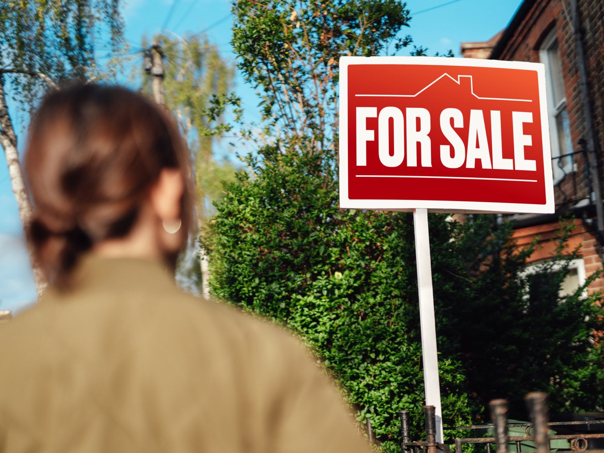 Woman looking at for sale sign outside property