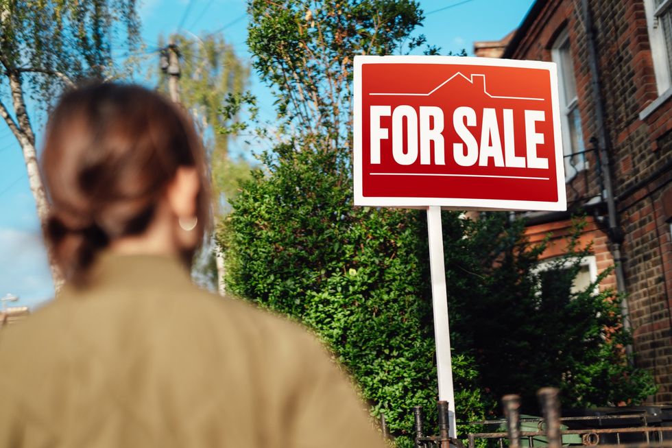 Woman looking at for sale sign outside property
