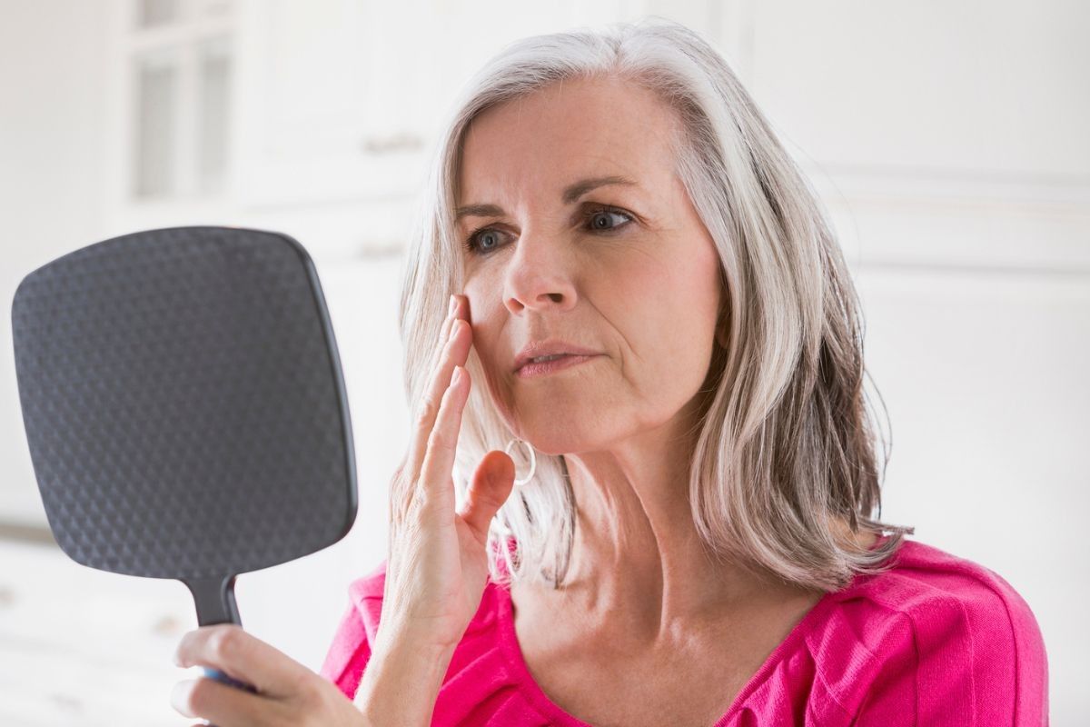 Woman looking at her face in mirror, touching cheek