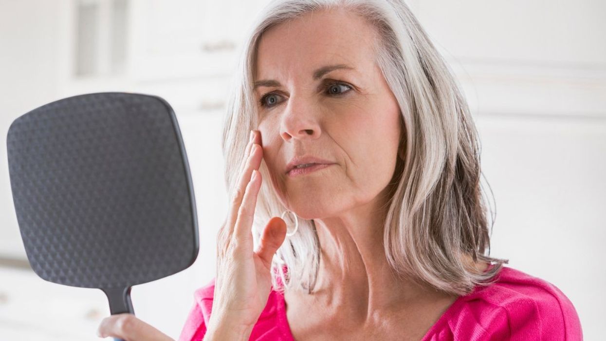 Woman looking at her face in mirror, touching cheek