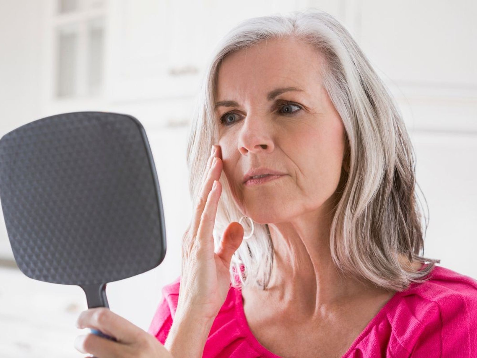 Woman looking at her face in mirror, touching cheek