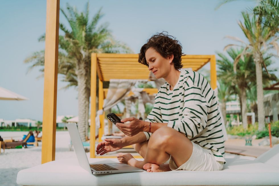 Woman on holiday, using phone and laptop