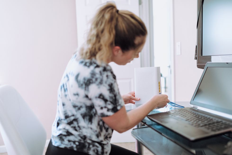 Woman plugging in a WiFi router at home by her laptop