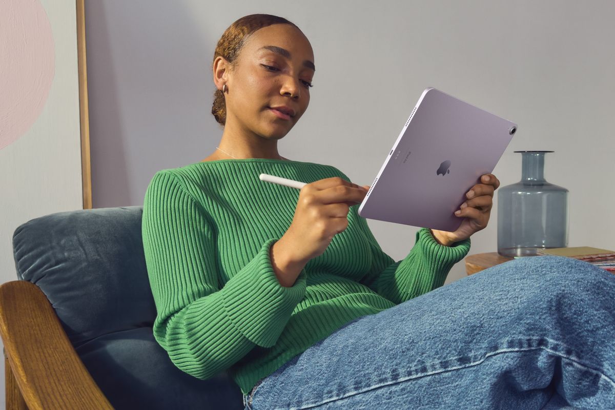 woman sitting reclined in a chair with the purple ipad air 2024 and an apple pencil stylus 