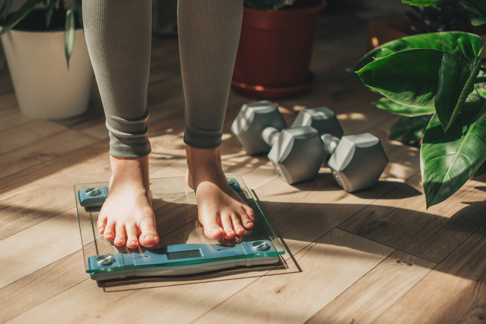 Woman standing on a weight scale by two dumbbells