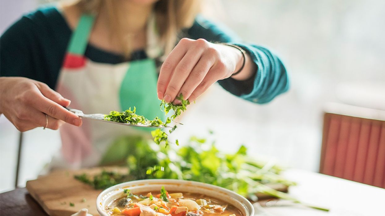 Woman throwing chopped parsley into soup
