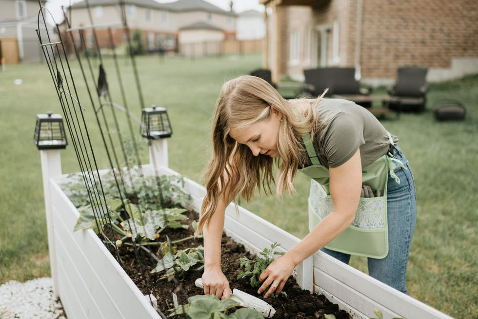Woman using a shovel to plant a flower in a wooden planter outside