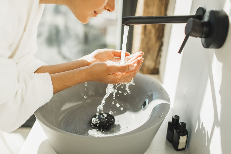 Woman waring a white bathrobe washing her face