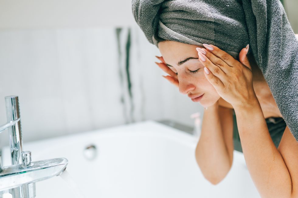 Woman washing her face, applying skin care by a sink