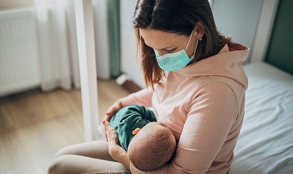 Woman wearing a face mask cuddling her newborn